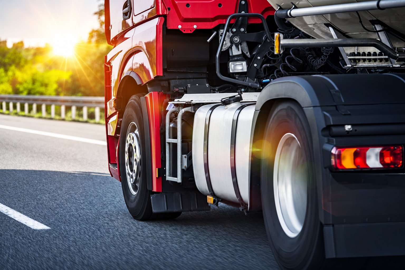 Camion rouge roulant sur l'autoroute au coucher du soleil, vue rapprochée de l'arrière du tracteur routier avec son réservoir chromé.