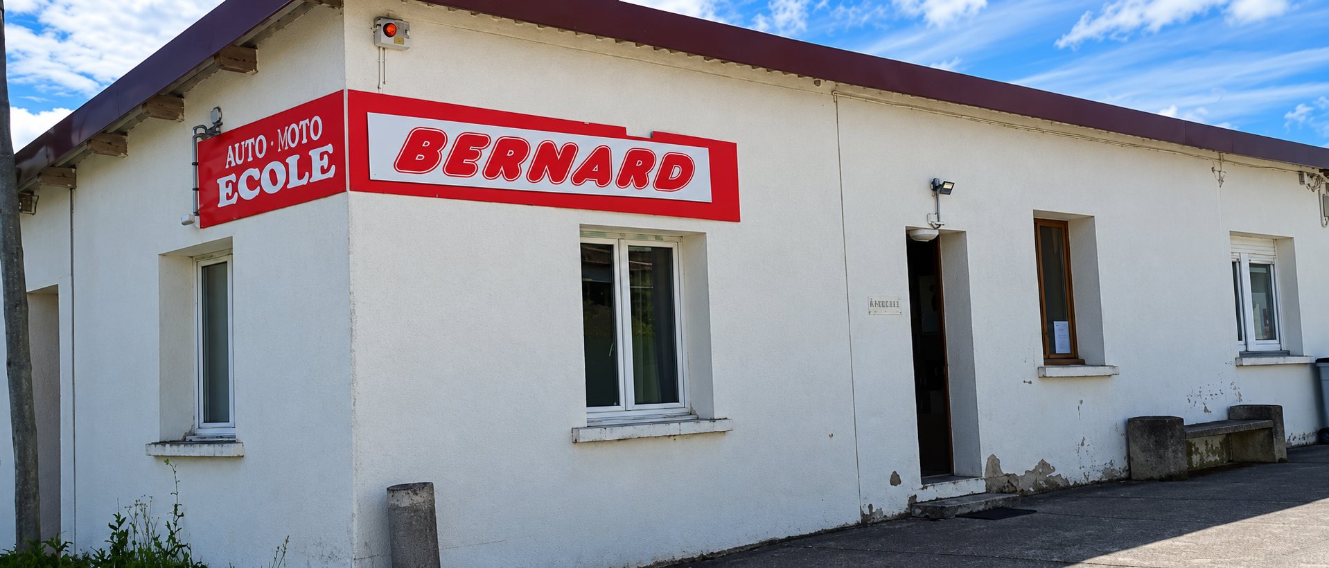 Façade blanche de l’auto-moto école Bernard avec son enseigne rouge et son panneau « Auto Moto École ».